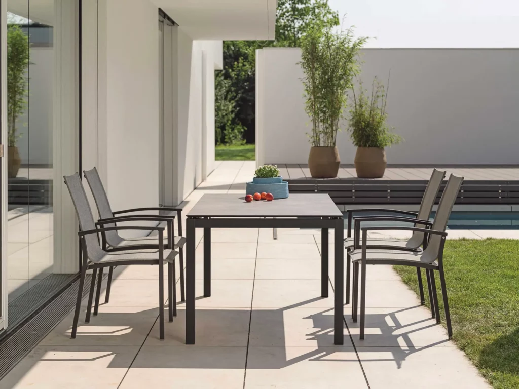 Vier STERN EVOEE Stapelsessel mit hoher Rückenlehne in Anthrazit und Textil um modernen Esstisch auf großzügiger Terrasse mit Pool, zeitgenössische Gartenarchitektur mit minimalistischen Designelementen