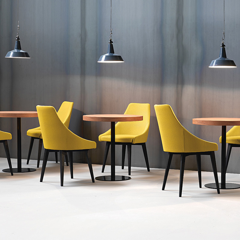 Armlehnstuhl Modell KONTEA 590 von Et al. – designstarker Polsterstuhl mit hoher Rückenlehne für moderne Restaurants und Cafés - Hantermann - Der Hotelausstatter Mehrere gelb gepolsterte KONTEA-590-Armlehnstühle mit schwarzen Holzbeinen an runden Holztischen unter industriellen Pendelleuchten