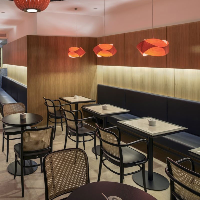 Bugholz Restaurantstuhl Modell 811 von TON – ikonischer Wiener Caféstuhl mit Armlehnen für stilvolle Gastronomie - Hantermann - Der Hotelausstatter Bugholz Restaurantstühle Modell 811 von TON mit Wiener Geflecht, dunklen Tischen und roten Pendelleuchten in modernem Café