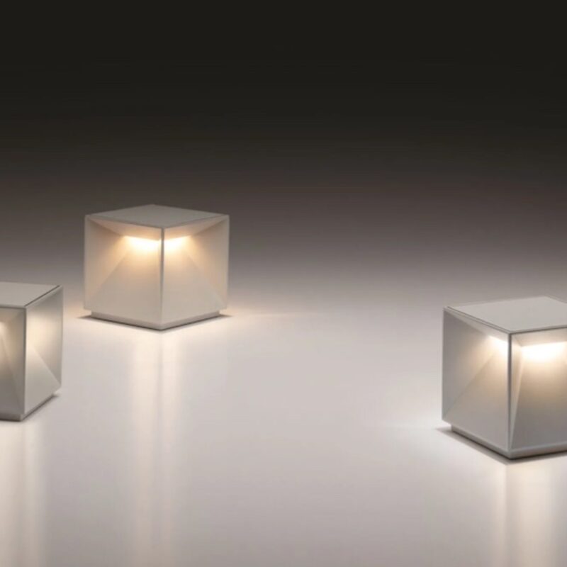 CUBIQ Akku Tischleuchte – Moderne kabellose LED-Leuchte - Hantermann - Der Hotelausstatter Drei moderne CUBIQ Akku Tischleuchten in Weiß mit würfelförmigem Design, geometrischen Lichtflächen und warmweißem Licht auf hellem Hintergrund