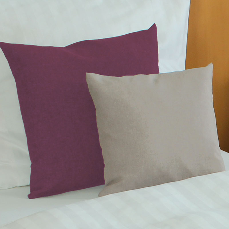 Dekokissen in Beere und Sand – elegante Farbkombination auf weißer Hotelbettwäsche - Hantermann - Der Hotelausstatter Zwei Dekokissen auf weißer Bettwäsche: ein größeres Kissen in Beereton im Hintergrund und ein kleineres sandfarbenes Kissen davor
