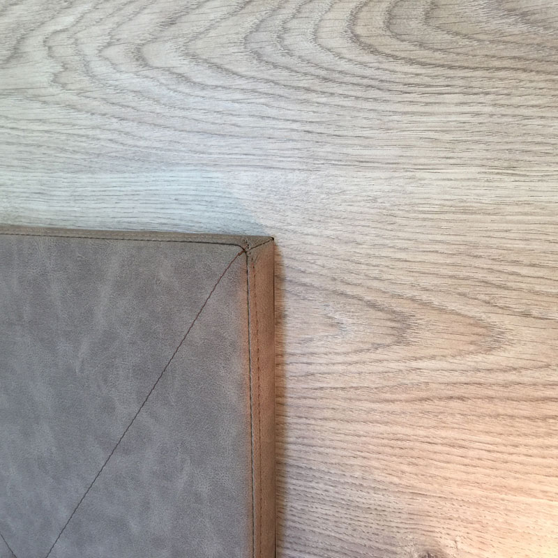 Detail LYONBED Boxspringbett KÜMMERSBRUCK SUPERIOR – präzise gearbeitete Kopfteilkante vor Holzpaneel - Hantermann - Der Hotelausstatter Nahaufnahme der oberen Ecke des gepolsterten Kopfteils des LYONBED Boxspringbett KÜMMERSBRUCK SUPERIOR vor heller Holzrückwand
