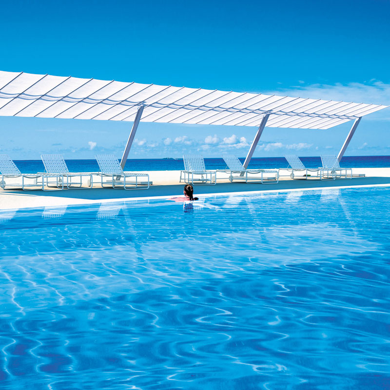 FLEXY Sonnenschutz von FIM mit weißem Stoff über Sonnenliegen an einem Pool mit Meerblick