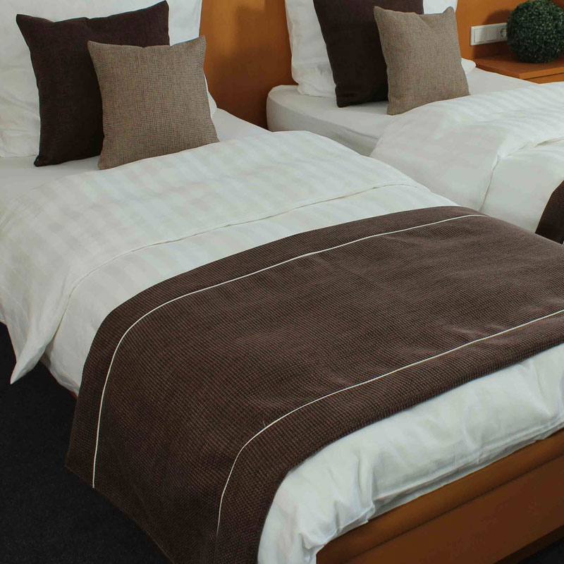 Hotel-Bettläufer und Dekokissen in Braun – stilvolle Akzente fürs Gästezimmer - Hantermann - Der Hotelausstatter Zwei Hotelbetten mit weißen Bezügen, braunen Bettläufern und passenden Dekokissen in einem warm gestalteten Gästezimmer