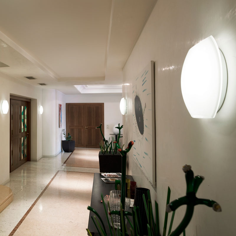 Hotel-Wandleuchte LARA als elegante Flurbeleuchtung - Hantermann - Der Hotelausstatter Hotel-Wandleuchte LARA aus mundgeblasenem Muranoglas in Weiß mit sanfter Beleuchtung an einer hellen Wand in einem eleganten Hotelflur
