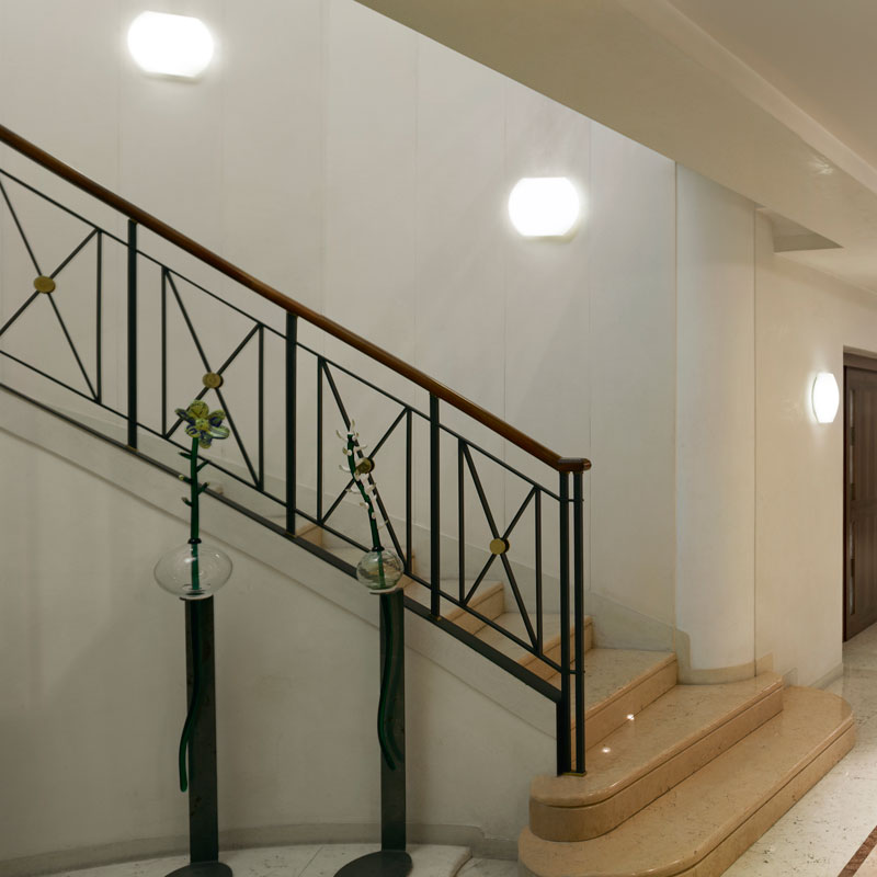 Hotel-Wandleuchte LARA – Beleuchtung im Treppenhaus - Hantermann - Der Hotelausstatter Hotel-Wandleuchte LARA aus mundgeblasenem Muranoglas als stilvolle Treppenhausbeleuchtung mit mehreren weiß leuchtenden Wandlampen entlang einer Treppe mit Metallgeländer