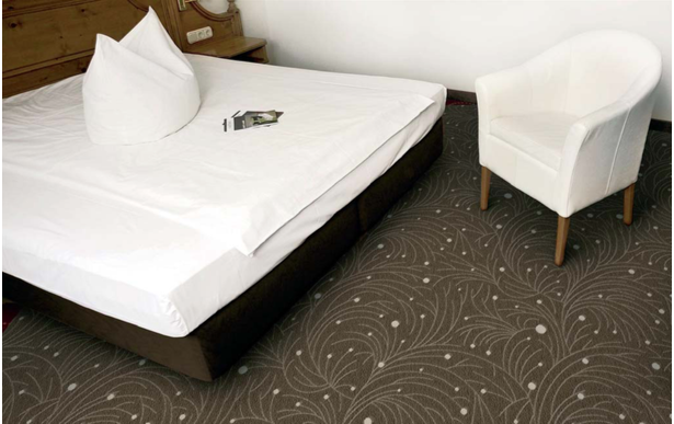 Hotelteppich 04 – floraler Teppich in Braun für Gästezimmer & Suiten - Hantermann - Der Hotelausstatter Hotelzimmer mit braunem Hotelteppich 04 im floralen Dessin und weißem Sessel