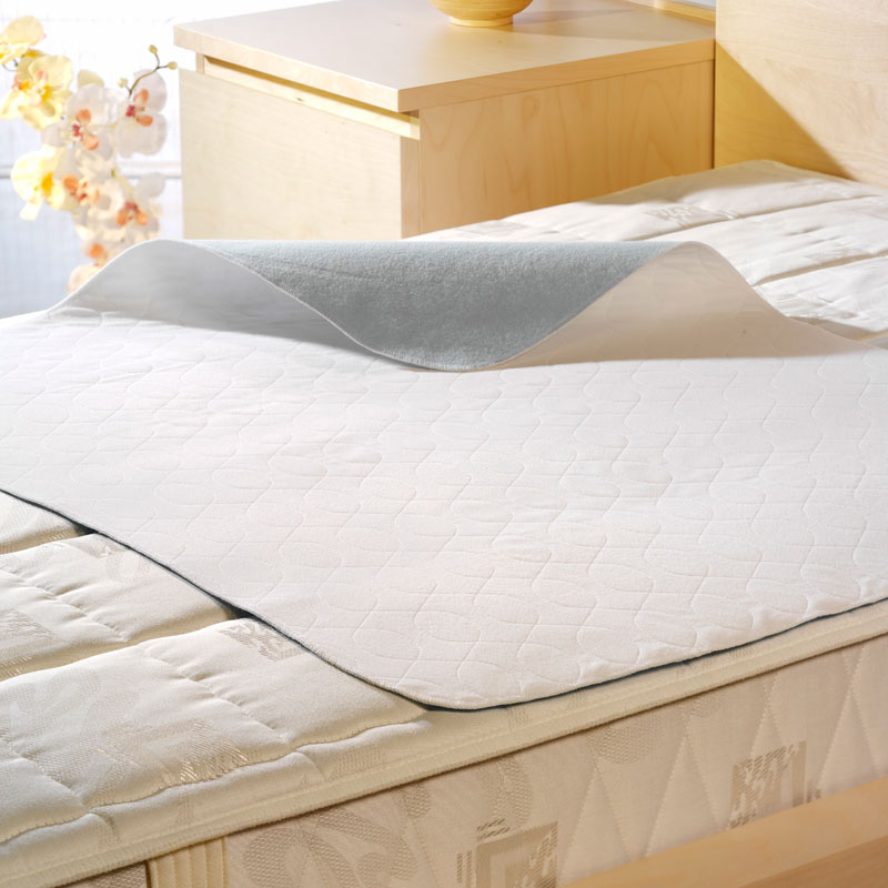 Weiße Inkontinenz-Mehrwegunterlage aus PE-Velours mit grauer Rückseite als Nässesperre auf einer Matratze im Schlafzimmer