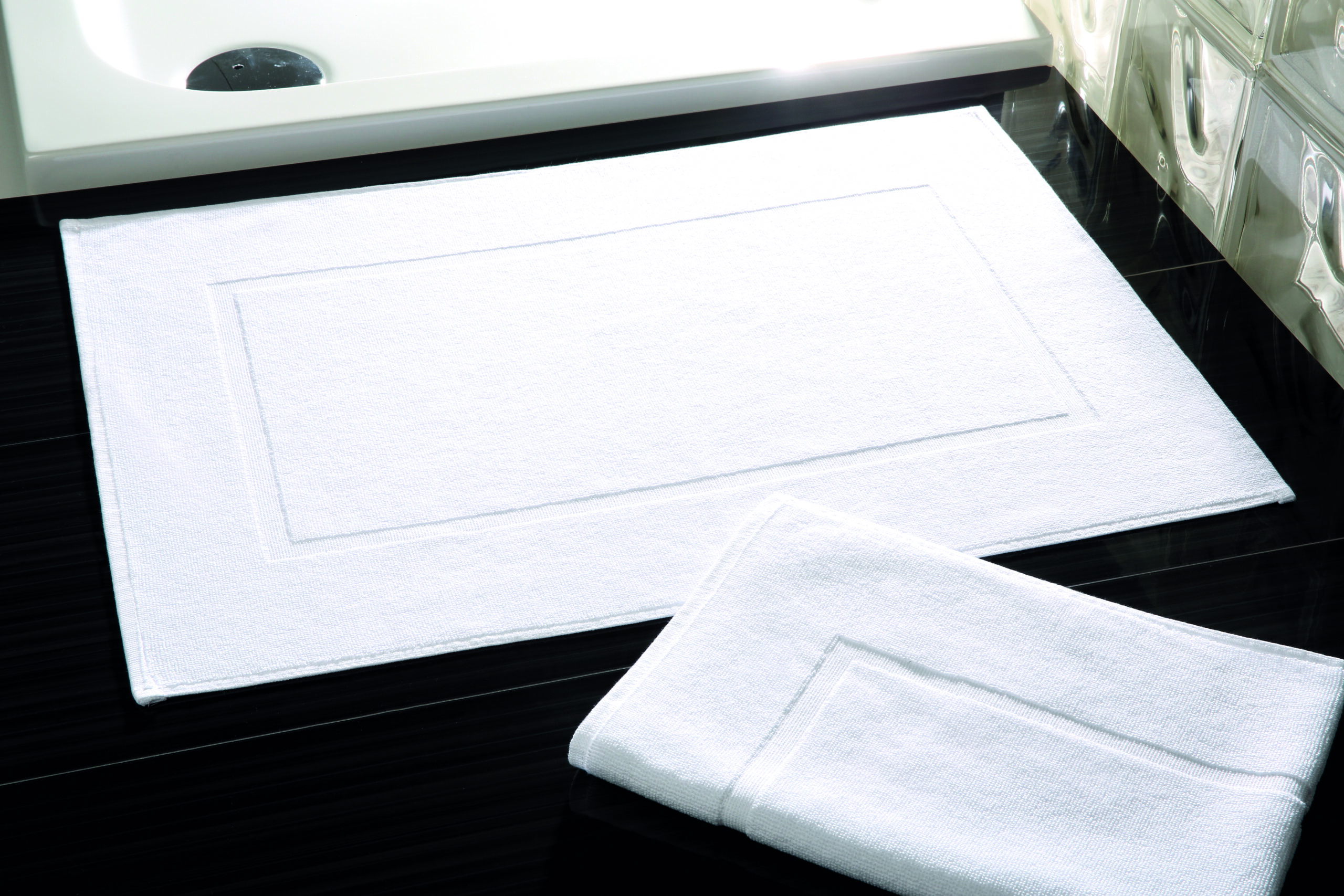 LESBOS Badvorleger 50×70 cm – 600 g/m² Walkfrottier für komfortable Hotel- und Spa-Bäder - Hantermann - Der Hotelausstatter LESBOS Badvorleger 50×70 cm aus 600 g/m² Walkfrottier in Weiß vor Dusche im Hotelbad