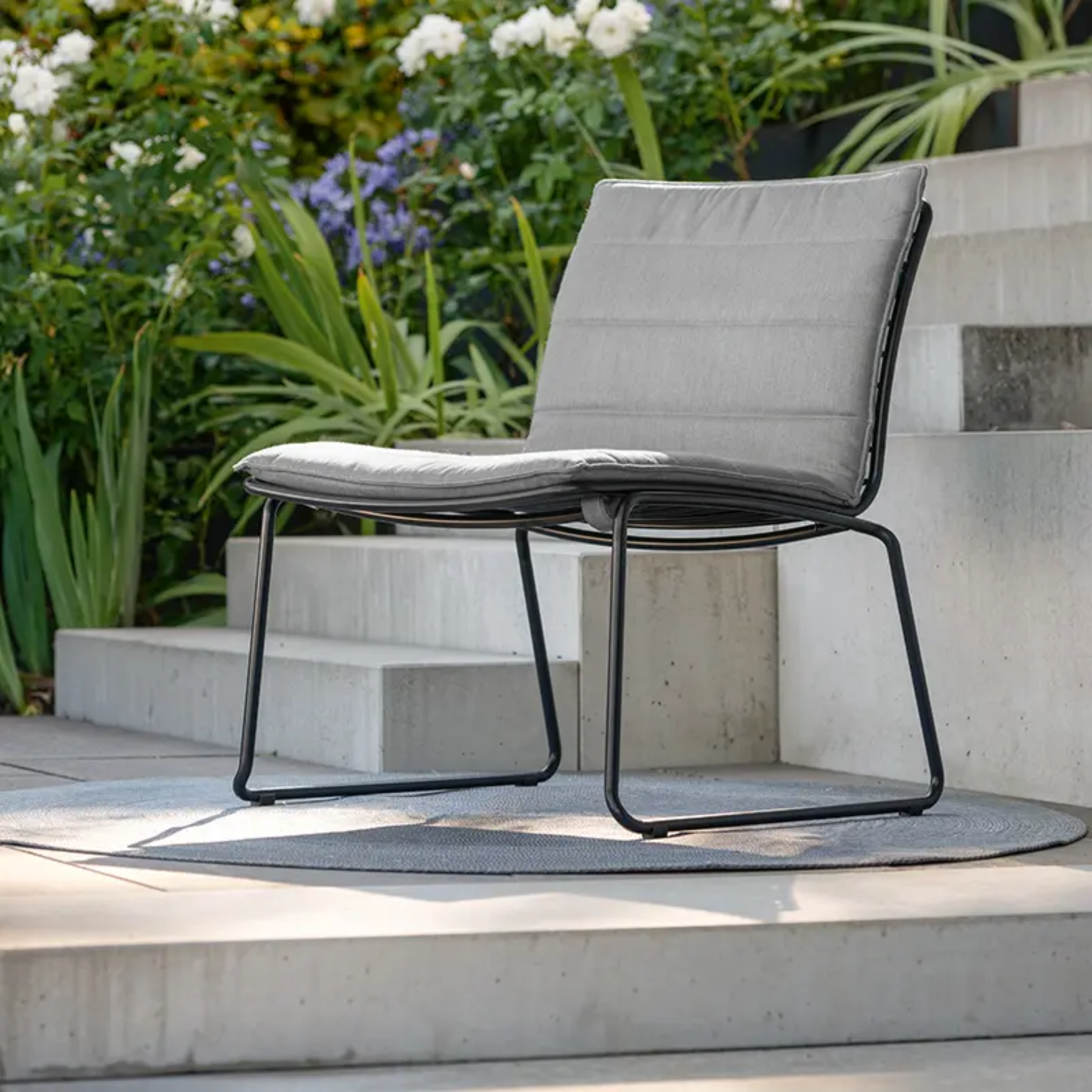 LEVI Lounge-Stapelstuhl von STERN® mit Sitzpolster - Hantermann - Der Hotelausstatter LEVI Outdoor Lounge-Stapelstuhl von STERN® in Schwarz mit grauem Sitzpolster im modernen Gartenbereich