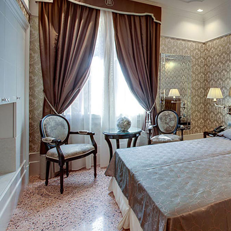 LUIGI 252S Louis XVI Stuhl – Eleganter Klassiker für Hotel & Restaurant - Hantermann - Der Hotelausstatter Zwei LUIGI-252S-Louis-XVI-Stühle mit ovaler Rückenlehne und gepolsterter Sitzfläche in einem klassisch eingerichteten Hotelzimmer vor Fenstern