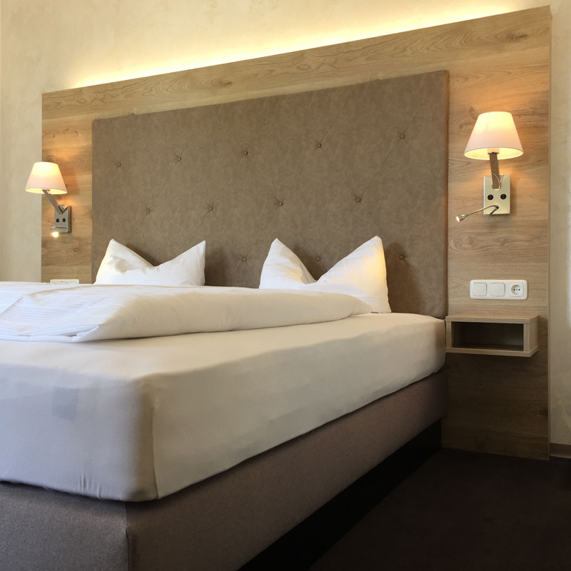 LYONBED Boxspringbett KÜMMERSBRUCK SUPERIOR – komfortables Hotelbett mit großem Polsterkopfteil - Hantermann - Der Hotelausstatter LYONBED Boxspringbett KÜMMERSBRUCK SUPERIOR mit hohem, rautenförmig gestepptem Kopfteil, beidseitigen Wandleuchten und weißer Bettwäsche