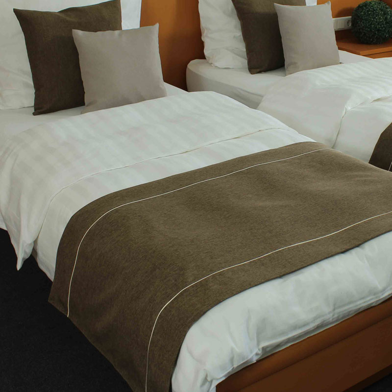 MIO Bettläufer/Fußplaid – ruhige Naturtöne auf weißer Hotelbettwäsche - Hantermann - Der Hotelausstatter Zwei Hotelbetten mit weißer Bettwäsche und MIO Bettläufer in warmem Braun, dazu passende braune und sandfarbene Dekokissen