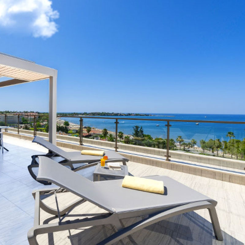 Moderne Sonnenliegen mit grauer Liegefläche auf einer Hotelterrasse mit Meerblick, Sonnenterrasse und blauem Himmel