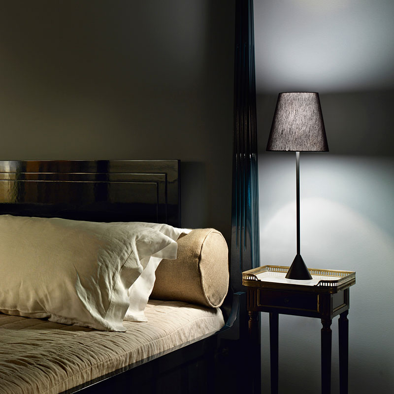 Nachttischlampe LYNDA – Elegante Tischleuchte in Schwarz - Hantermann - Der Hotelausstatter Moderne Nachttischlampe LYNDA mit schwarzem konischem Lampenschirm, schlankem Leuchtenstab und kegelförmigem Standfuß auf einem eleganten Nachttisch neben einem Bett
