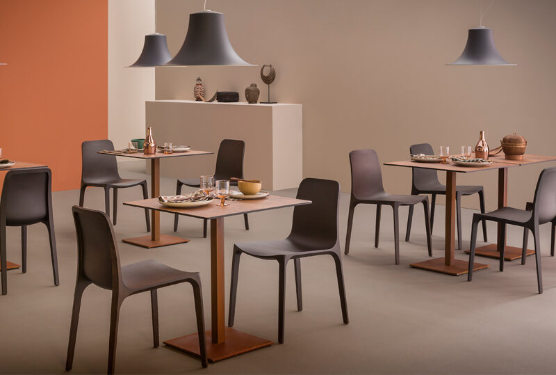 Vier graue PEDRALI L004S Pendelleuchten mit geschwungenen Lampenschirmen über gedeckten Restauranttischen mit grauen Stühlen und orangefarbener Wand