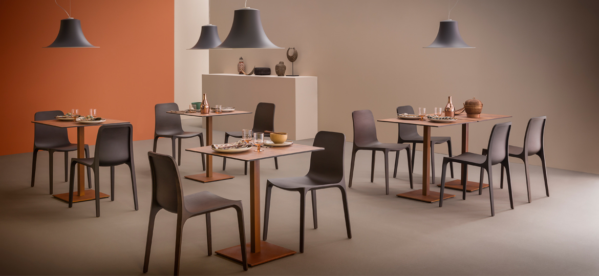PEDRALI L004S Pendelleuchte in modernem Restaurantambiente - Hantermann - Der Hotelausstatter Vier graue PEDRALI L004S Pendelleuchten mit geschwungenen Lampenschirmen über gedeckten Restauranttischen mit grauen Stühlen und orangefarbener Wand