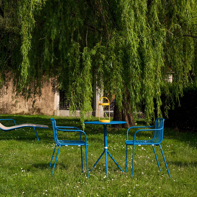Pedrali NOLITA 3655 – Blaue Outdoor-Sessel im grünen Gartenambiente - Hantermann - Der Hotelausstatter Blaue NOLITA 3655 Outdoor Stapelsessel von Pedrali mit Tisch in einem begrünten Außenbereich