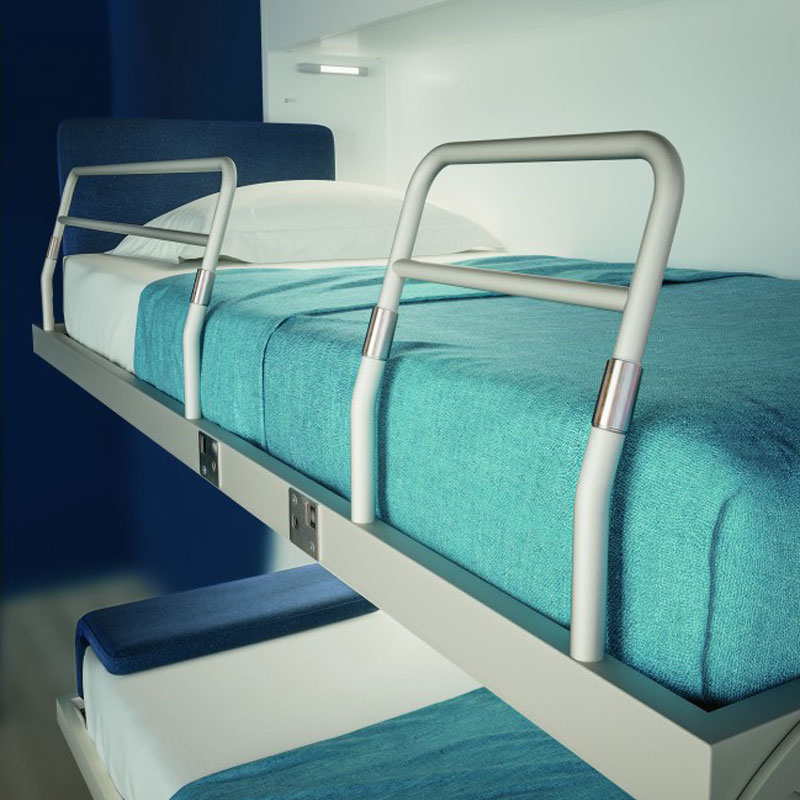 Schrankbett KAY DUO – Detailansicht des oberen Etagenbetts - Hantermann - Der Hotelausstatter Nahaufnahme des oberen Betts im Schrankbett KAY DUO mit türkisfarbener Decke, weißem Kissen, blauer Rückenlehne und silbergrauer Absturzsicherung