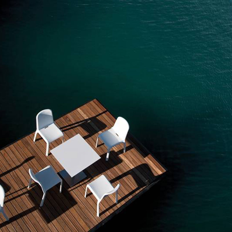 SNOW 300 Outdoor Stapelstuhl von Pedrali – weiße Kunststoffstühle für Steg, Strandbar & Seeterrassen - Hantermann - Der Hotelausstatter Mehrere weiße SNOW 300 Outdoor Stapelstühle von Pedrali mit quadratischem Tisch auf einem Holzsteg über dem Wasser