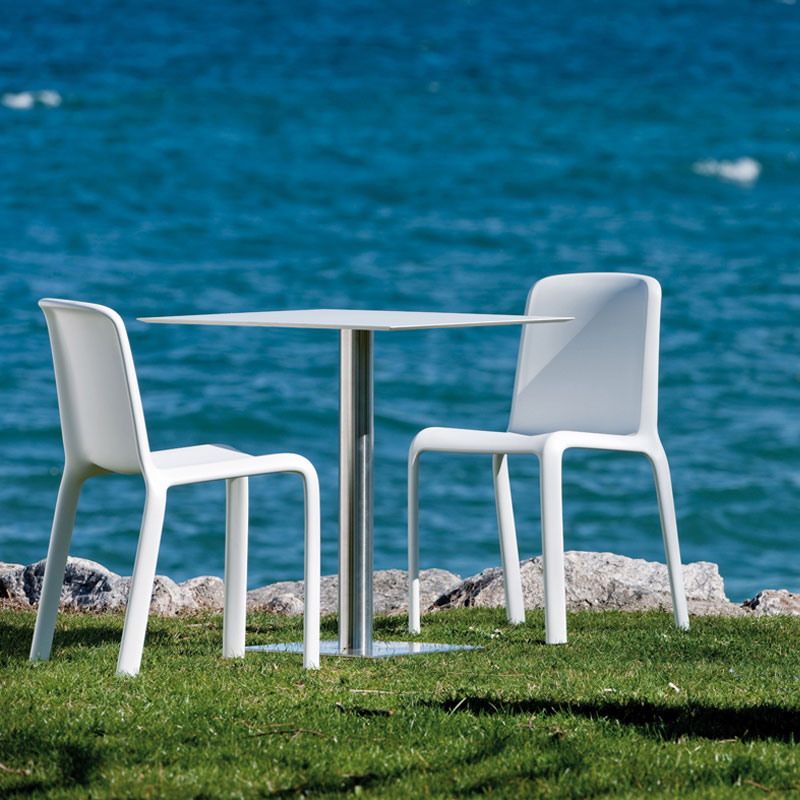 SNOW 300 Outdoor Stapelstuhl von Pedrali – weiße Kunststoffstühle für Strandbar, Seeterrasse & Hotelgarten - Hantermann - Der Hotelausstatter Zwei weiße SNOW 300 Outdoor Stapelstühle von Pedrali an einem Bistrotisch auf der Wiese vor dem Meer, Kunststoffstuhl für Außenbereiche