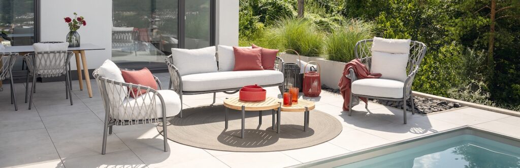 Moderne Pool-Lounge mit grauer Rattanmöbel, cremefarbenen Polstern und Rostrot-Akzenten.