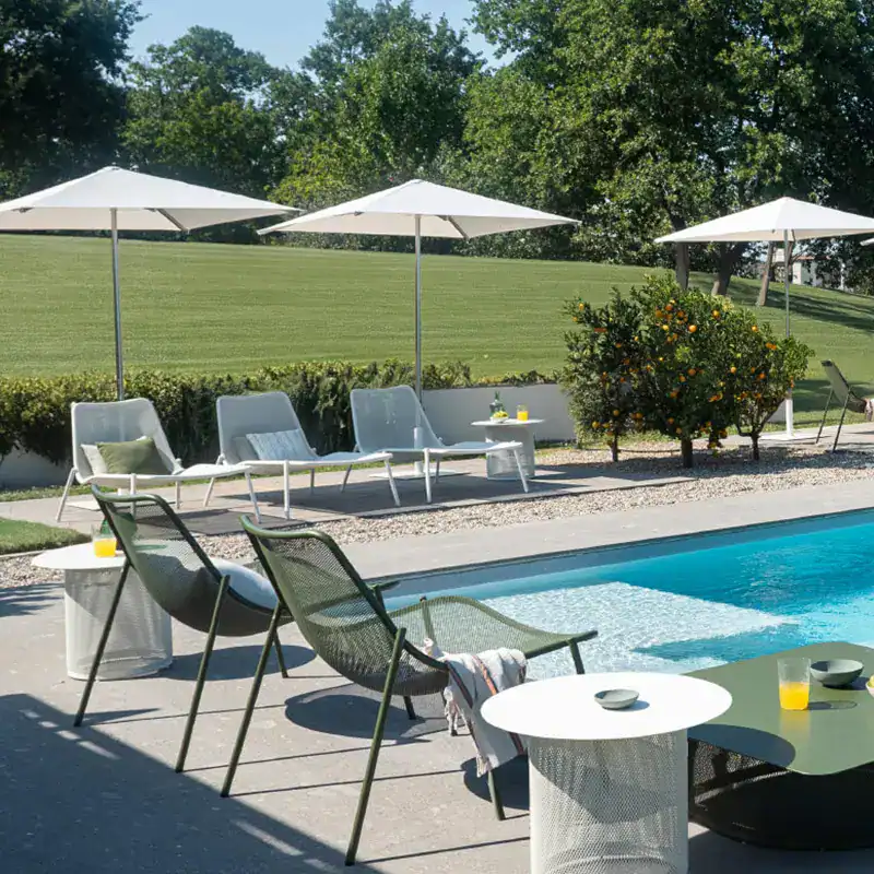 verschiedene Sonnenliegen von emu am Pool mit Sonnenschirmen und grünem rasen