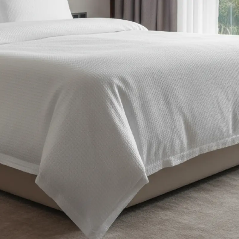 Das Bild zeigt ein Hotelbett, das mit weißer Seersucker-Bettwäsche bezogen ist. Die typische Krepp-Struktur ist deutlich zu erkennen und sorgt für eine edle, moderne Optik. Die Bettdecke fällt locker über die Bettkante und unterstreicht den frischen, gepflegten Eindruck der Hotelzimmerausstattung.