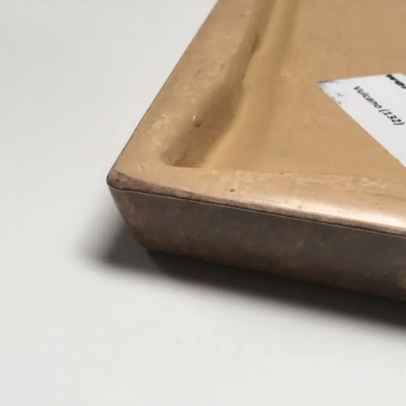 Das Bild zeigt eine Detailaufnahme einer Tischplatte aus Werzalit, bei der vor allem die Kanten- und Profilgestaltung sichtbar ist. Die Oberfläche ist mit einem hellbraunen Stein- oder Metalldekor versehen und die Platte besitzt eine charakteristisch abgerundete Kante mit einer eingelassenen Mulde auf der Unterseite. Das Material wirkt massiv und robust – ideal für stark beanspruchte Einsatzbereiche wie Gastronomie, Hotel oder Outdoor. Das Foto betont die Verarbeitungsqualität und die Funktionalität dieser speziellen Objekt-Tischplatte.