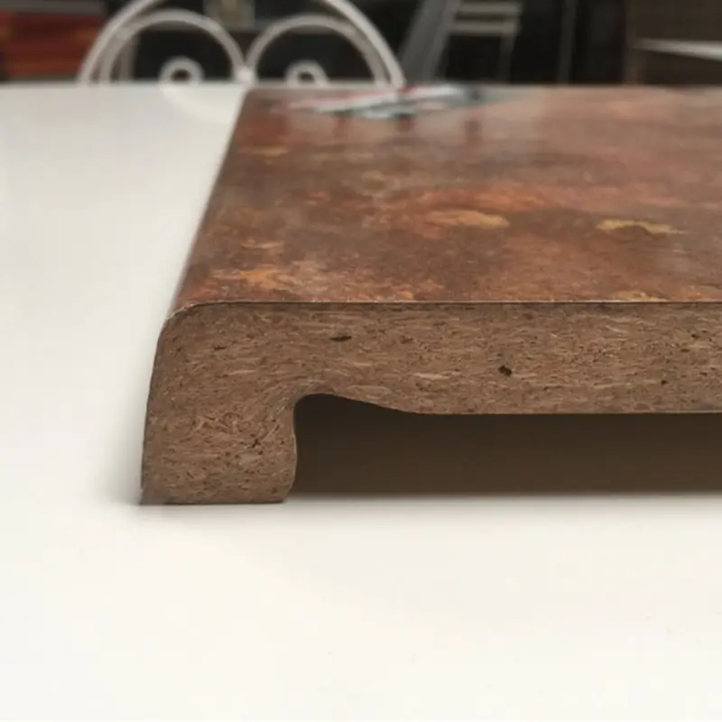 Das Bild zeigt eine Tischplatte im Querschnitt, bei der Struktur und Material deutlich sichtbar sind. Die Oberseite besitzt eine braun-rustikale Dekoroberfläche, die von Werzalit typisch robust und pflegeleicht ist. Die Form der Platte ist speziell profiliert – mit einer markanten, abgerundeten Kante und einer Vertiefung darunter, was auf hohe Stabilität und Widerstandsfähigkeit hinweist. Der Querschnitt ermöglicht einen Blick auf den massiven Kern und stellt die Qualität für den Einsatz im Gastronomie- oder Objektbereich heraus.