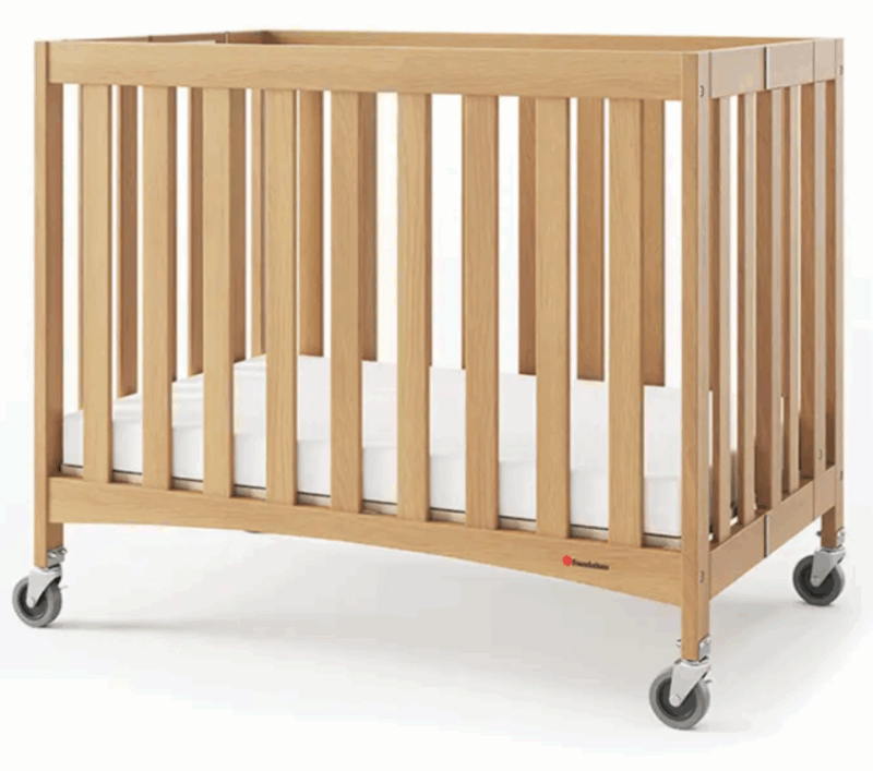 Das Bild zeigt ein kompaktes Babybett aus Holz mit einem klaren, minimalistischen Design. Material & Farbe: Natürliches Holz mit glatter Oberfläche und warmem Finish – wirkt hochwertig und freundlich Gitterstruktur: Alle vier Seiten sind mit vertikalen Holzstreben versehen, die für Sicherheit und gute Luftzirkulation sorgen Mobilität: Jedes Bein ist mit einem stabilen Rollenrad ausgestattet – insgesamt vier Rollen, zwei davon vermutlich feststellbar Matratze: Eine weiße Matratze liegt passgenau im Bett, wirkt sauber und bequem Das Bett ist für Kleinkinder gedacht, ideal für Hotels, Kitas oder den mobilen Einsatz. Die Kombination aus Funktionalität und schlichtem Design macht es besonders attraktiv für professionelle Umgebungen.