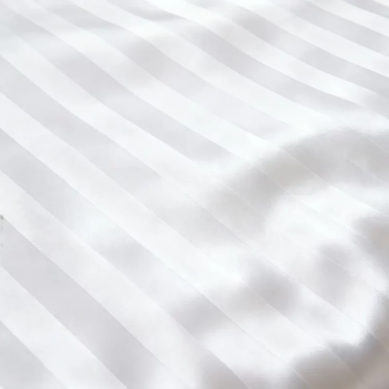 Das Bild zeigt einen Ausschnitt von weißer Streifsatin-Bettwäsche mit exakt parallelen, breiten 20 mm Streifen. Die strukturierte Oberfläche wirkt glatt, gleichmäßig und sauber.