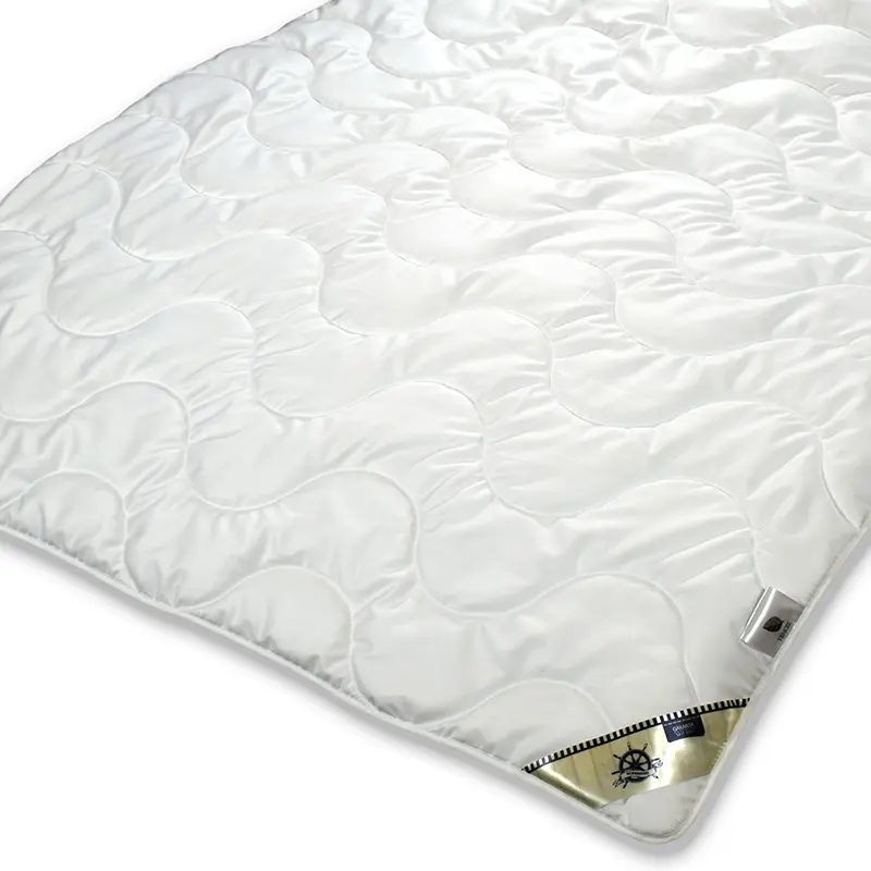 Garanta Summertime Tencel Sommerdecke – Extra-Leicht, natürliche & nachhaltige Naturfaserdecke - Hantermann - Der Hotelausstatter Garanta Summertime Tencel Sommerdecke Extra-Leicht, weiße Decke mit geschwungener Steppung und etikettierter Ecke im Vordergrund